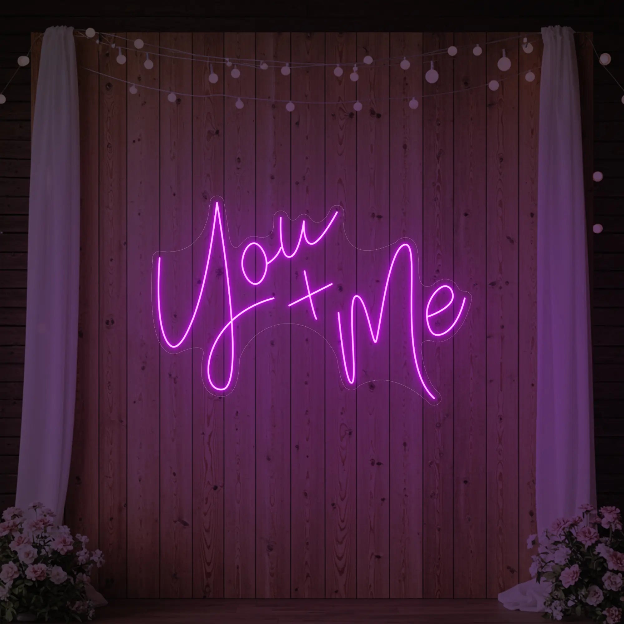 'You + Me' neon sign glowing in deep pink against a styled interior wall.