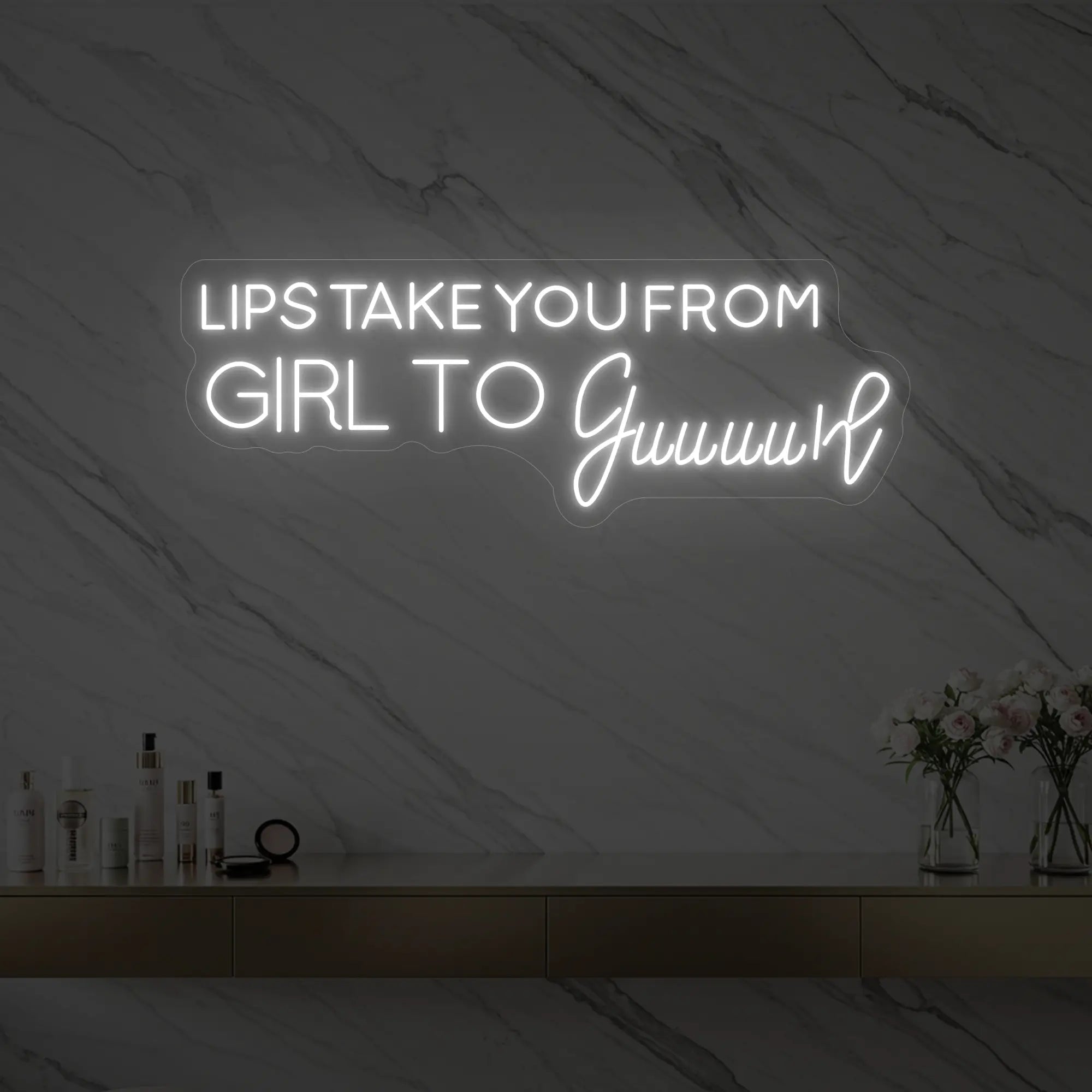 Photo of the 'LIPS TAKE YOU FROM GIRL TO Guuuurl' neon sign glowing in cool white against a styled interior wall.
