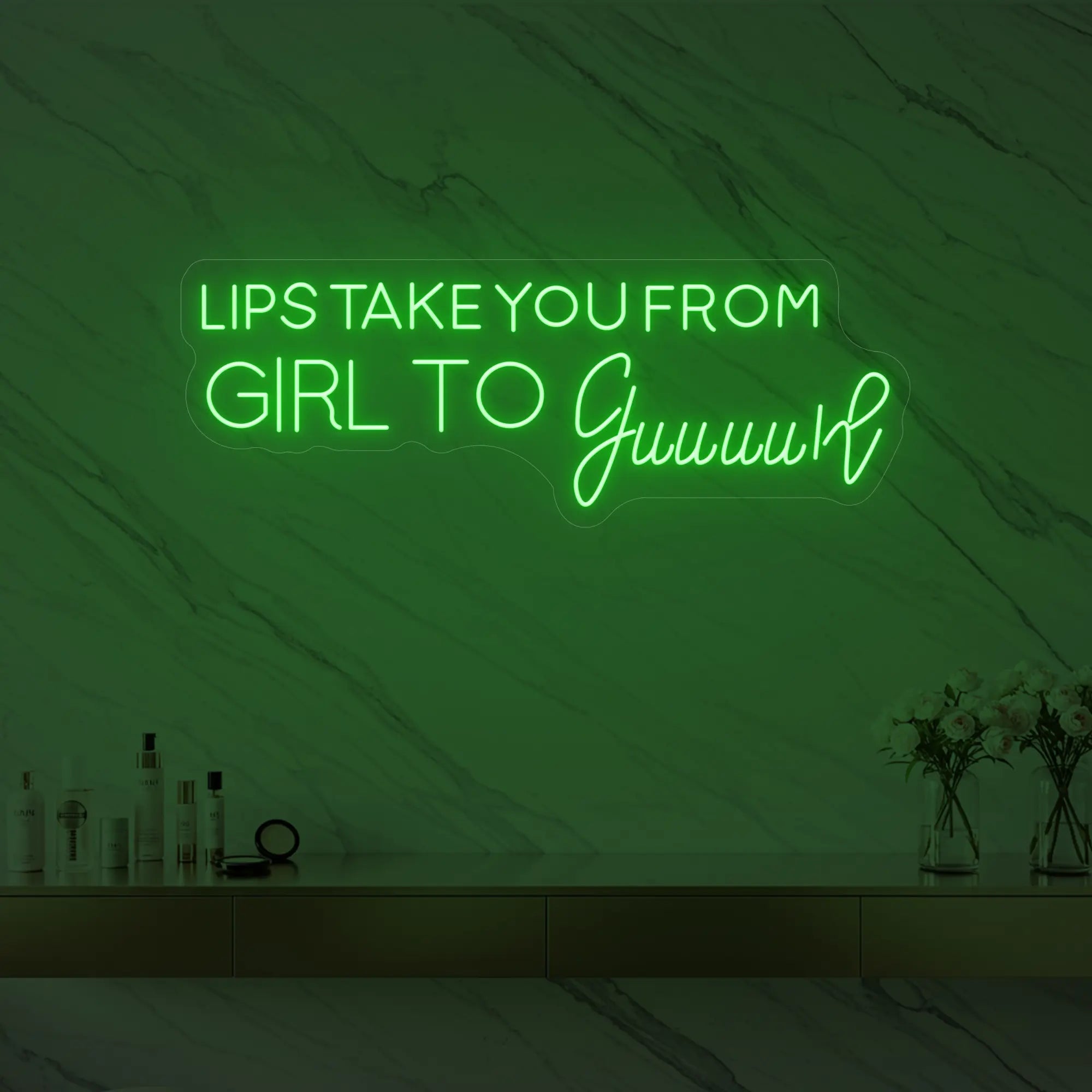 Photo of the 'LIPS TAKE YOU FROM GIRL TO Guuuurl' neon sign glowing in green against a styled interior wall.