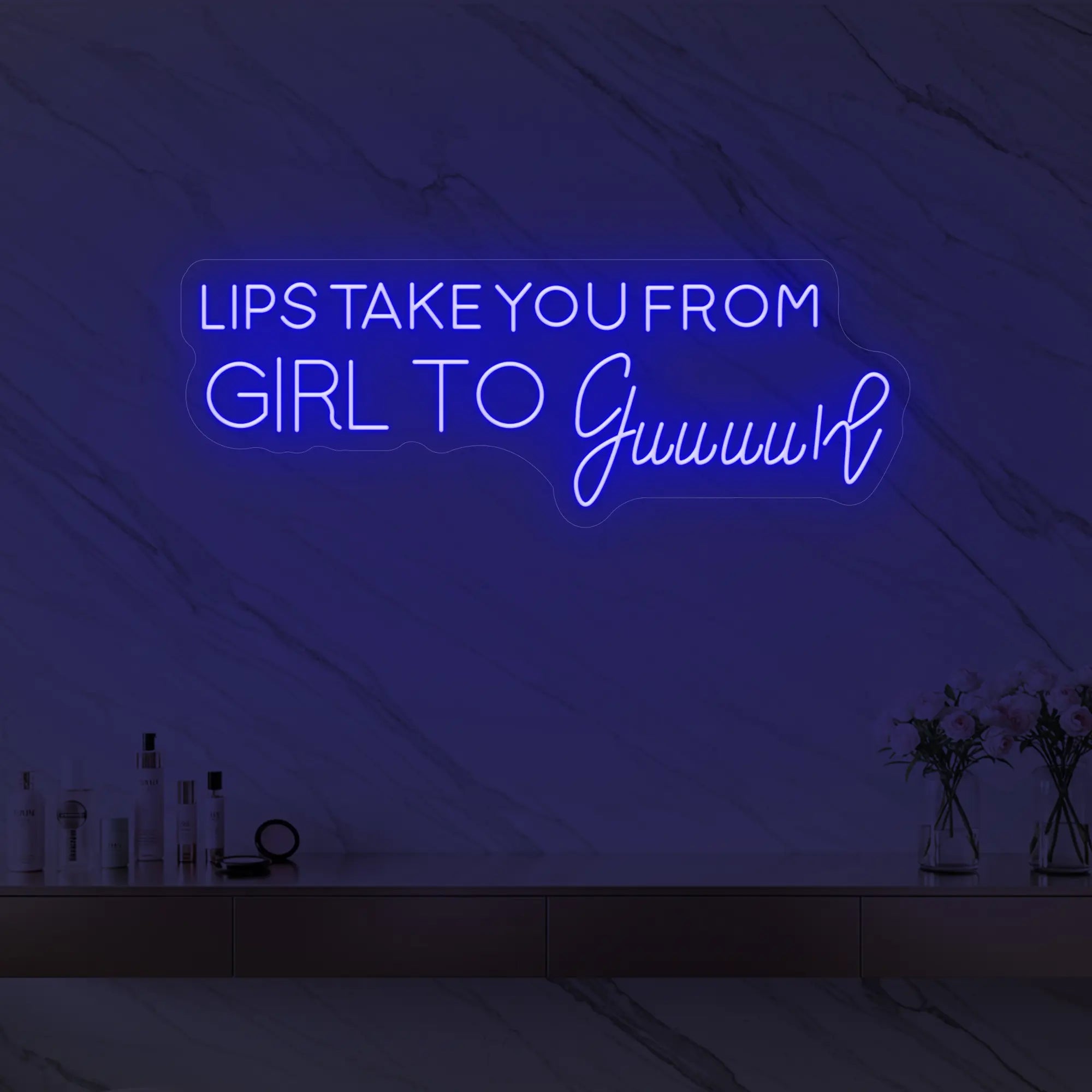 Photo of the 'LIPS TAKE YOU FROM GIRL TO Guuuurl' neon sign glowing in deep blue against a styled interior wall.