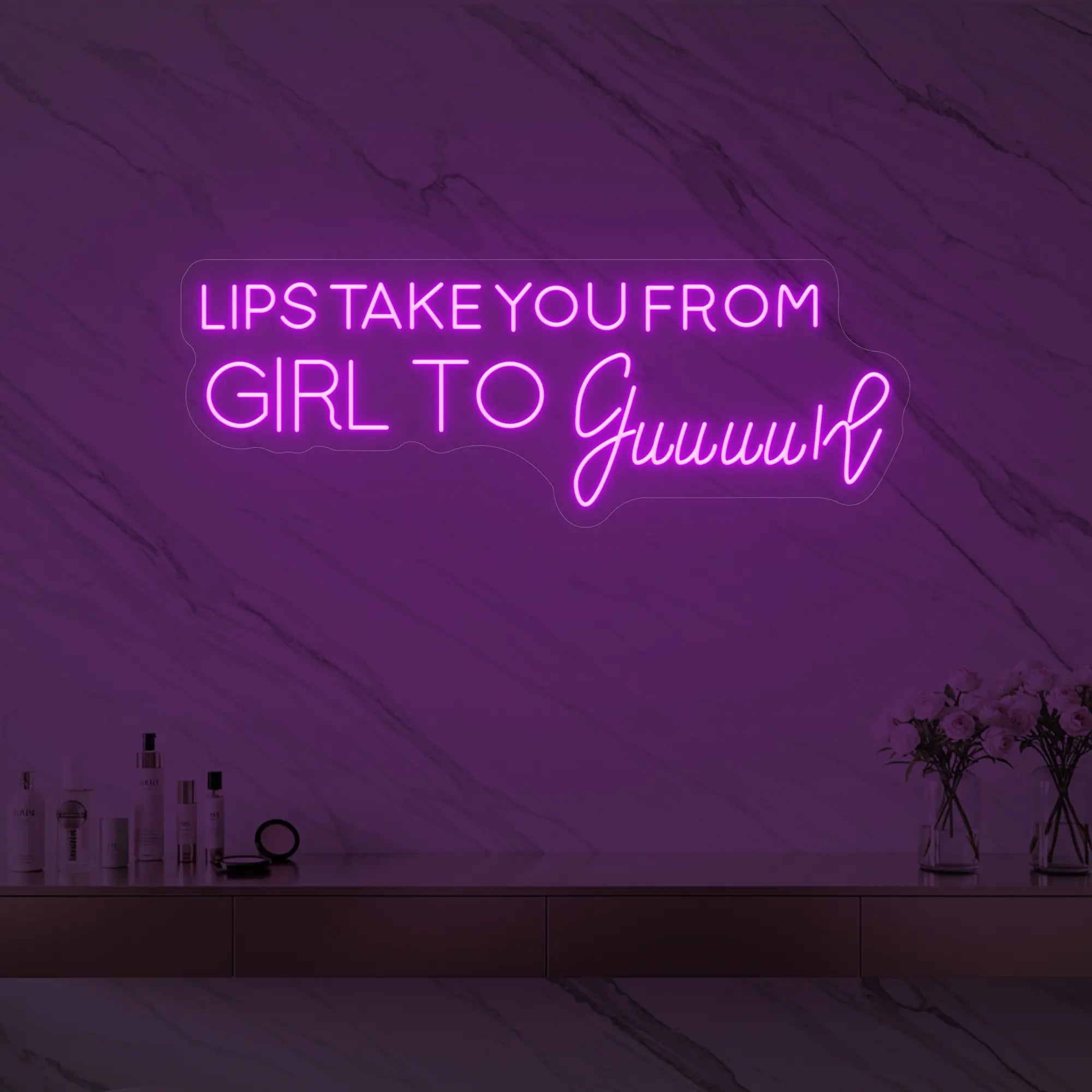 Photo of the 'LIPS TAKE YOU FROM GIRL TO Guuuurl' neon sign glowing in deep pink against a styled interior wall.