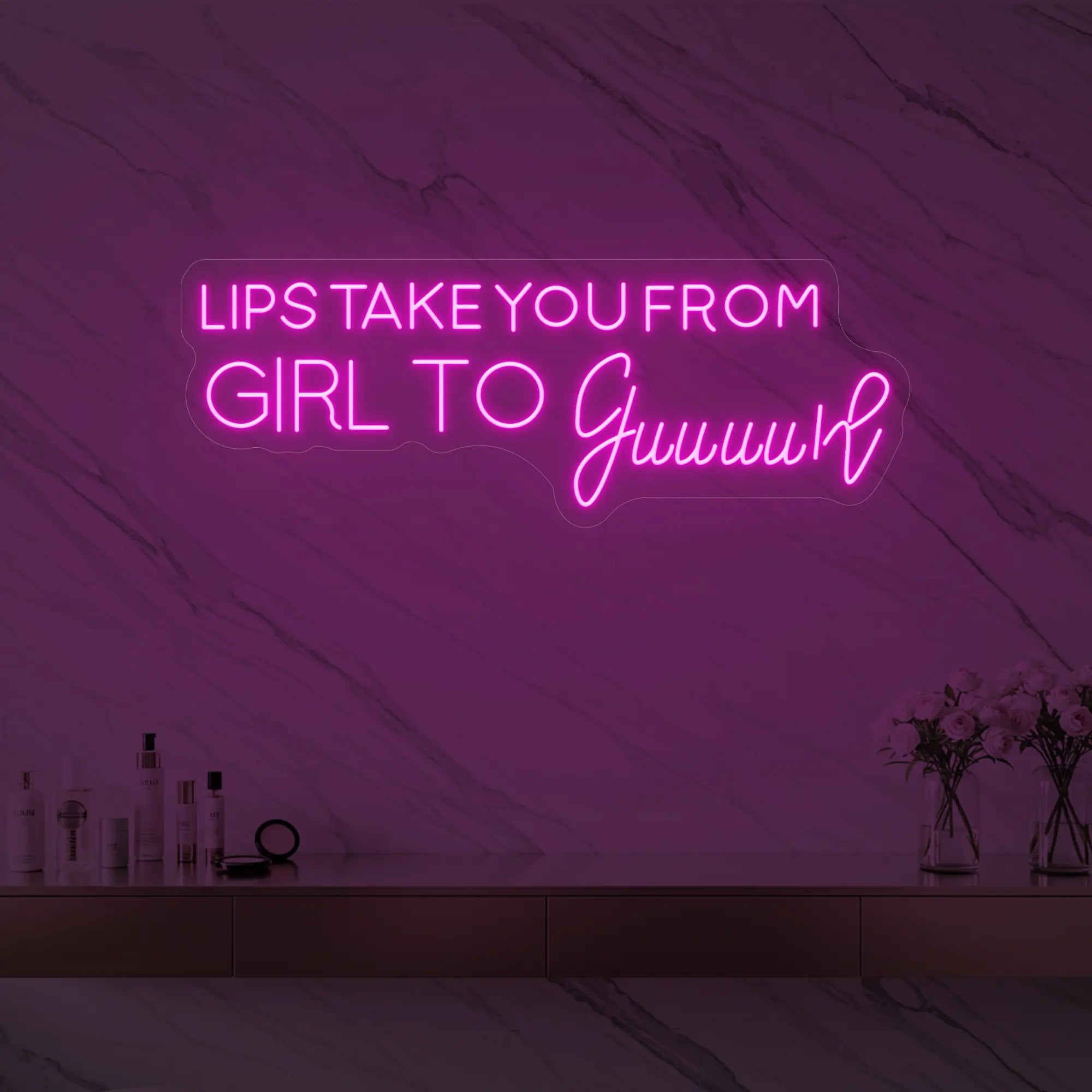 Photo of the 'LIPS TAKE YOU FROM GIRL TO Guuuurl' neon sign glowing in light pink against a styled interior wall.