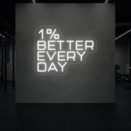 '1% Better Every Day' neon sign glowing in cool white against a styled interior wall.
