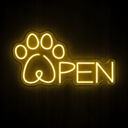 Open Paw LED Neon Sign featuring a glowing warm yellow paw print integrated with the word OPEN on clear acrylic backing, displayed against a dark wood wall for pet store and grooming business decor.