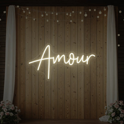 Photo of the 'Amour' neon sign glowing in warm white against a styled interior wall.