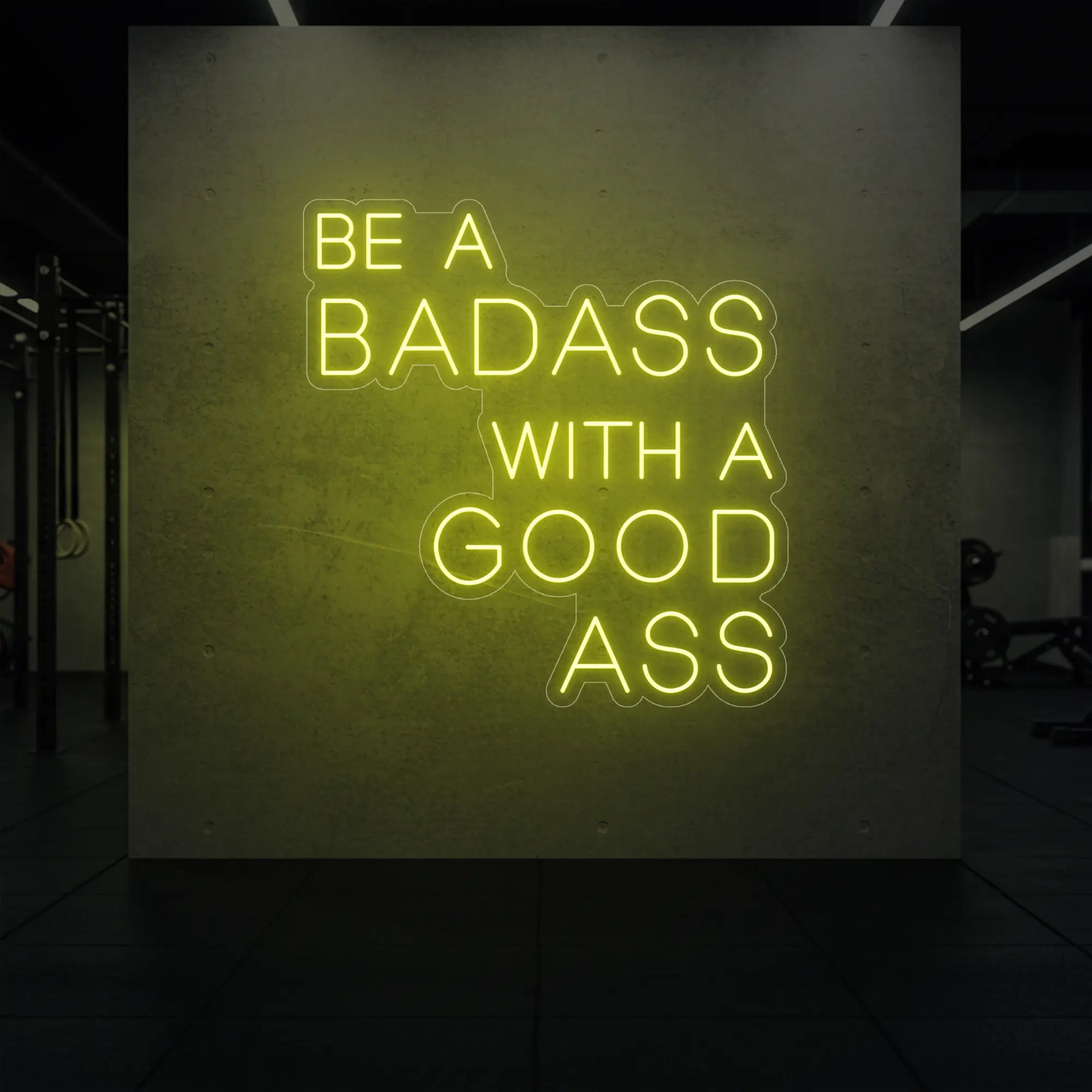 'Be a Badass With a Good Ass' neon sign glowing in lemon yellow against a styled interior wall.