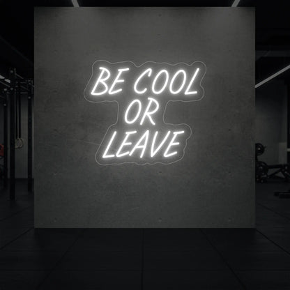  'Be Cool or Leave' neon sign glowing in cool white against a styled interior wall.