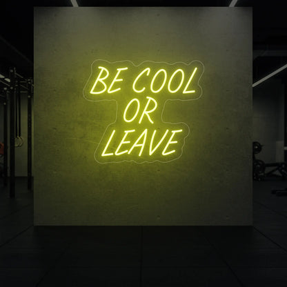 'Be Cool or Leave' neon sign glowing in lemon yellow against a styled interior wall.