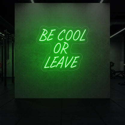 'Be Cool or Leave' neon sign glowing in green against a styled interior wall.