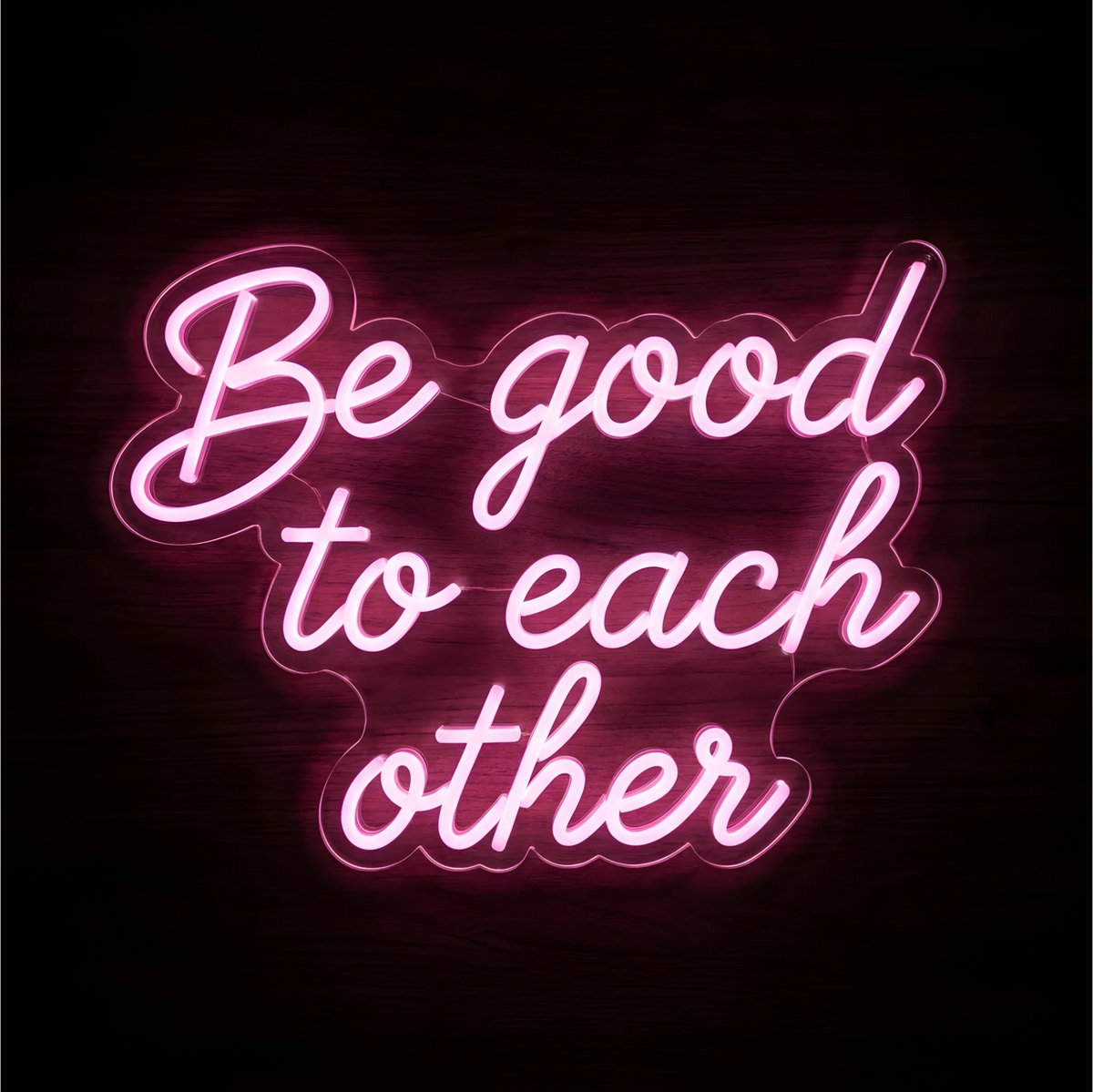 Be Good to Each Other LED Neon Sign in glowing pink script lettering on clear acrylic against a dark wood background, suited to living rooms and classrooms.