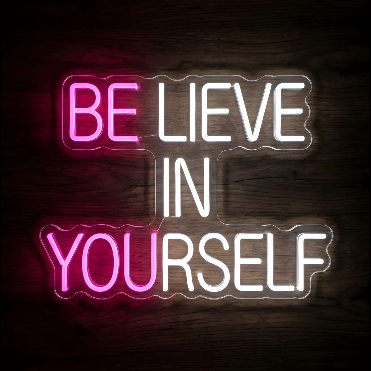 Believe in Yourself LED Neon Sign with “BE” and “YOU” glowing pink and the remaining uppercase lettering in white, displayed on clear acrylic against a dark wood background, suited to bedrooms and home offices.