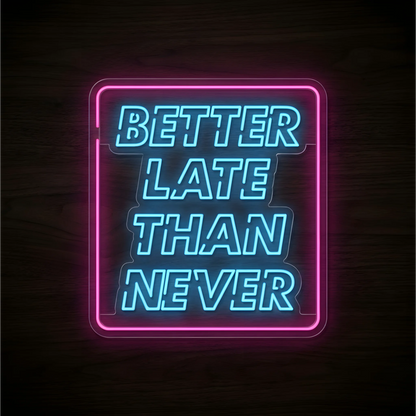 “BETTER LATE THAN NEVER” LED Neon Sign with bright blue lettering inside a pink rectangular neon outline on clear acrylic backing against a dark wood background, suitable for home offices and creative workspaces.
