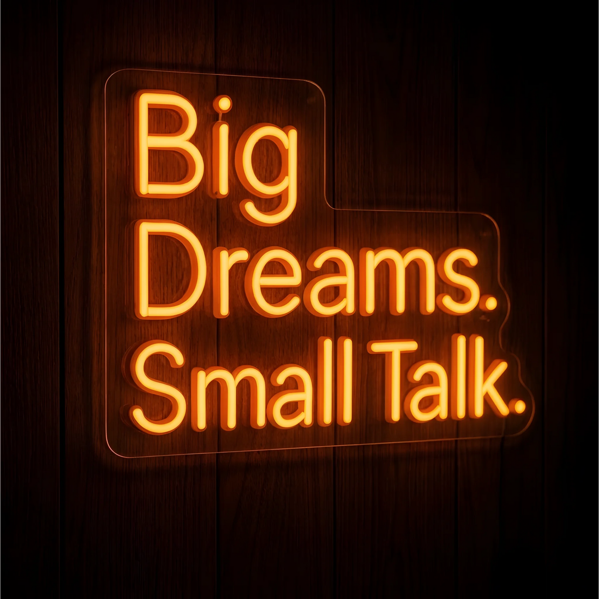 Big Dreams Small Talk LED Neon Sign featuring the words “Big Dreams. Small Talk.” in glowing orange lettering on clear acrylic backing against a dark wood background, ideal for home offices and creative workspaces.