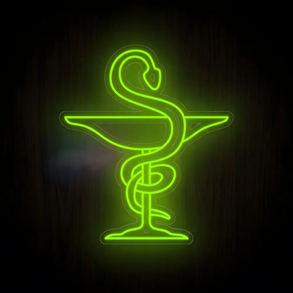 Green Bowl of Hygieia Pharmacy LED Neon Sign featuring a glowing serpent wrapped around a pharmacy bowl on clear acrylic backing against a dark wooden wall.