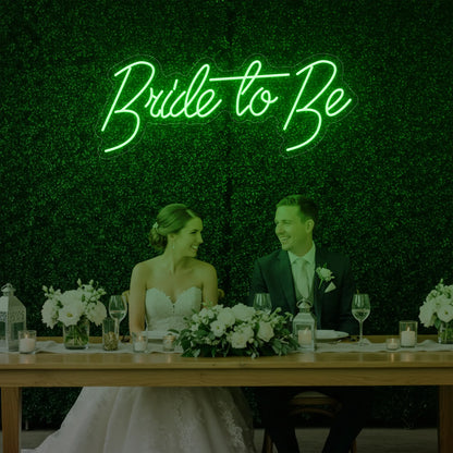 Photo of the 'Bride To Be' neon sign glowing in green against a styled interior wall.