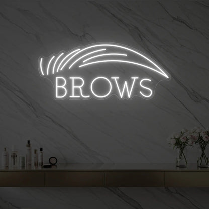 Photo of the 'BROWS' neon sign with an eyebrow graphic glowing in cool white against a styled interior wall.