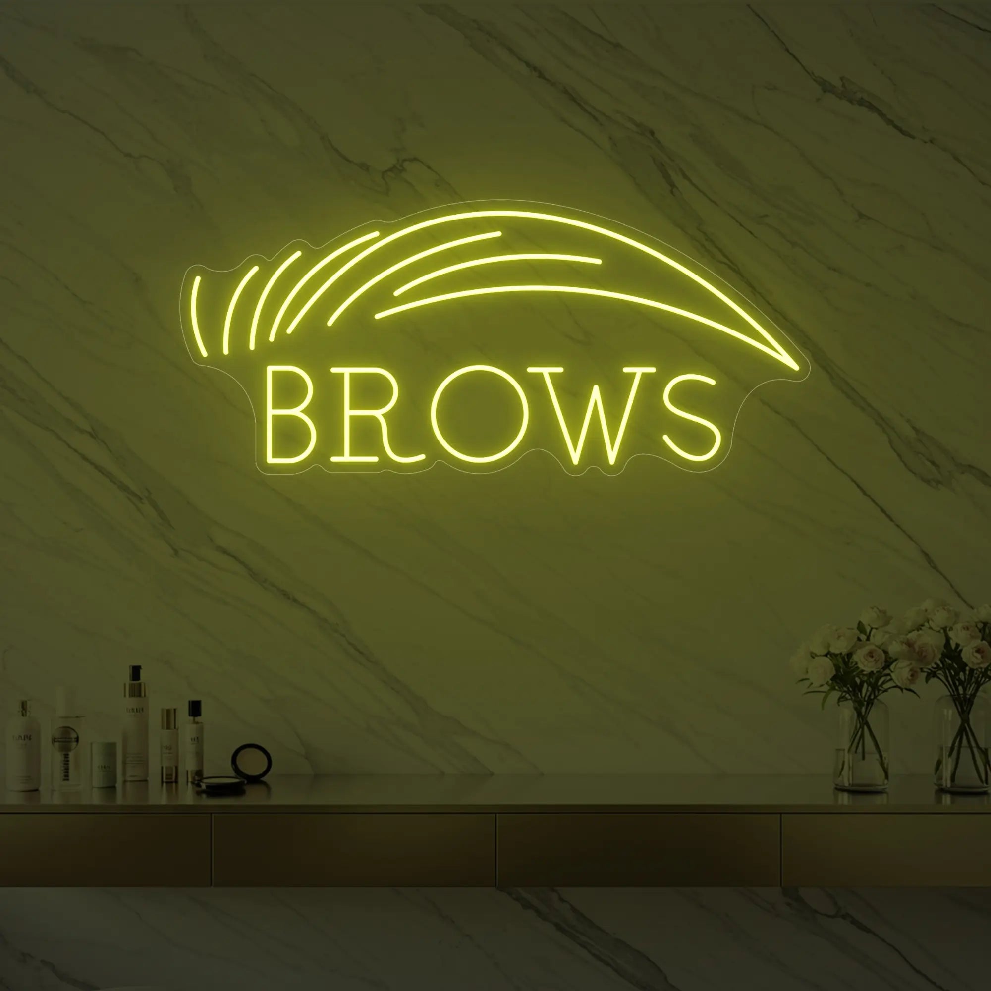 Photo of the 'BROWS' neon sign with an eyebrow graphic glowing in lemon yellow against a styled interior wall.