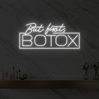 Photo of the 'But first, BOTOX' neon sign glowing in cool white against a styled interior wall.