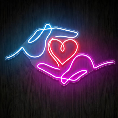 Caring Hands Heart LED Neon Sign featuring glowing blue and pink hands surrounding a bright red heart on clear cut-to-shape acrylic backing, displayed against a dark wooden wall.