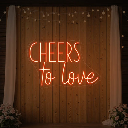 Photo of the 'Cheers To Love' neon sign glowing in golden yellow against a styled interior wall.