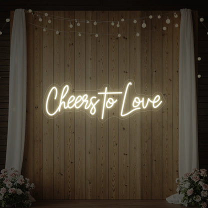 Photo of the 'Cheers To Love' neon sign glowing in warm white against a styled interior wall.