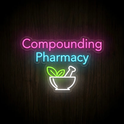 Compounding Pharmacy LED Neon Sign featuring pink Compounding lettering, cyan Pharmacy text, and a white mortar and pestle with green leaves on clear cut-to-shape acrylic against a dark wooden wall.