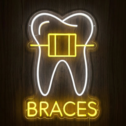 Dental Braces LED neon sign featuring a glowing white tooth outline with yellow orthodontic braces and BRACES lettering on clear acrylic backing against a dark wooden wall.