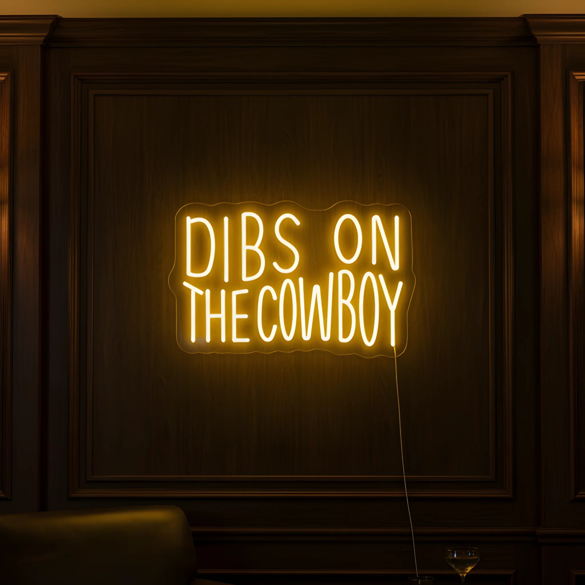 Photo of the 'Dibs on the Cowboy' neon sign glowing in yellow against a western-inspired interior wall.