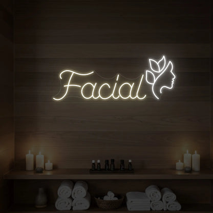 Photo of the 'Facial' neon sign with a botanical face silhouette glowing in warm white against a styled interior wall.