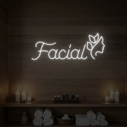 Photo of the 'Facial' neon sign with a botanical face silhouette glowing in cool white against a styled interior wall.