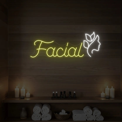 Photo of the 'Facial' neon sign with a botanical face silhouette glowing in lemon yellow against a styled interior wall.