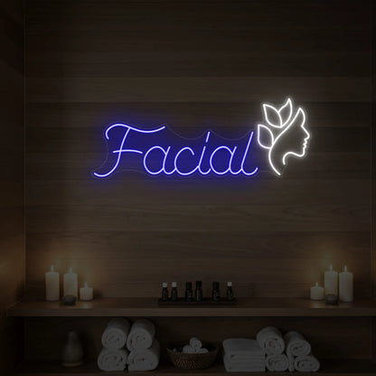 Photo of the 'Facial' neon sign with a botanical face silhouette glowing in deep blue against a styled interior wall.