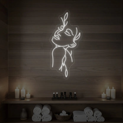 Photo of the 'Flower Girl' neon sign featuring a minimalist face and leaf line art glowing in cool white against a styled interior wall.