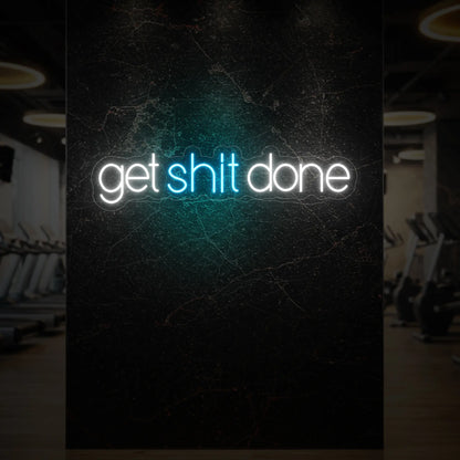  'Get Shit Done' neon sign glowing in ice blue against a styled interior wall.