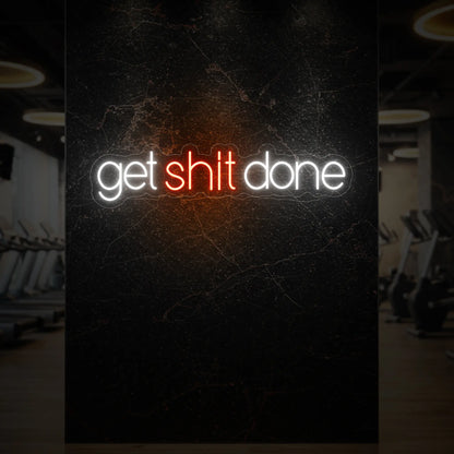 'Get Shit Done' neon sign glowing in golden yellow against a styled interior wall.