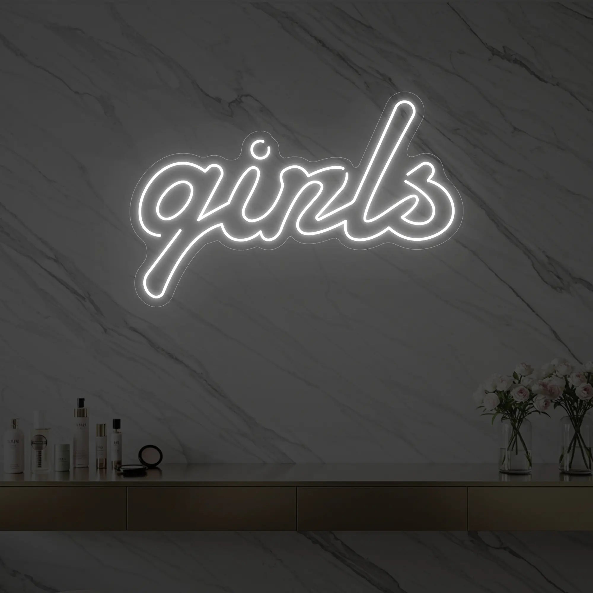 Photo of the 'girls' neon sign in playful script glowing in cool white against a styled interior wall.