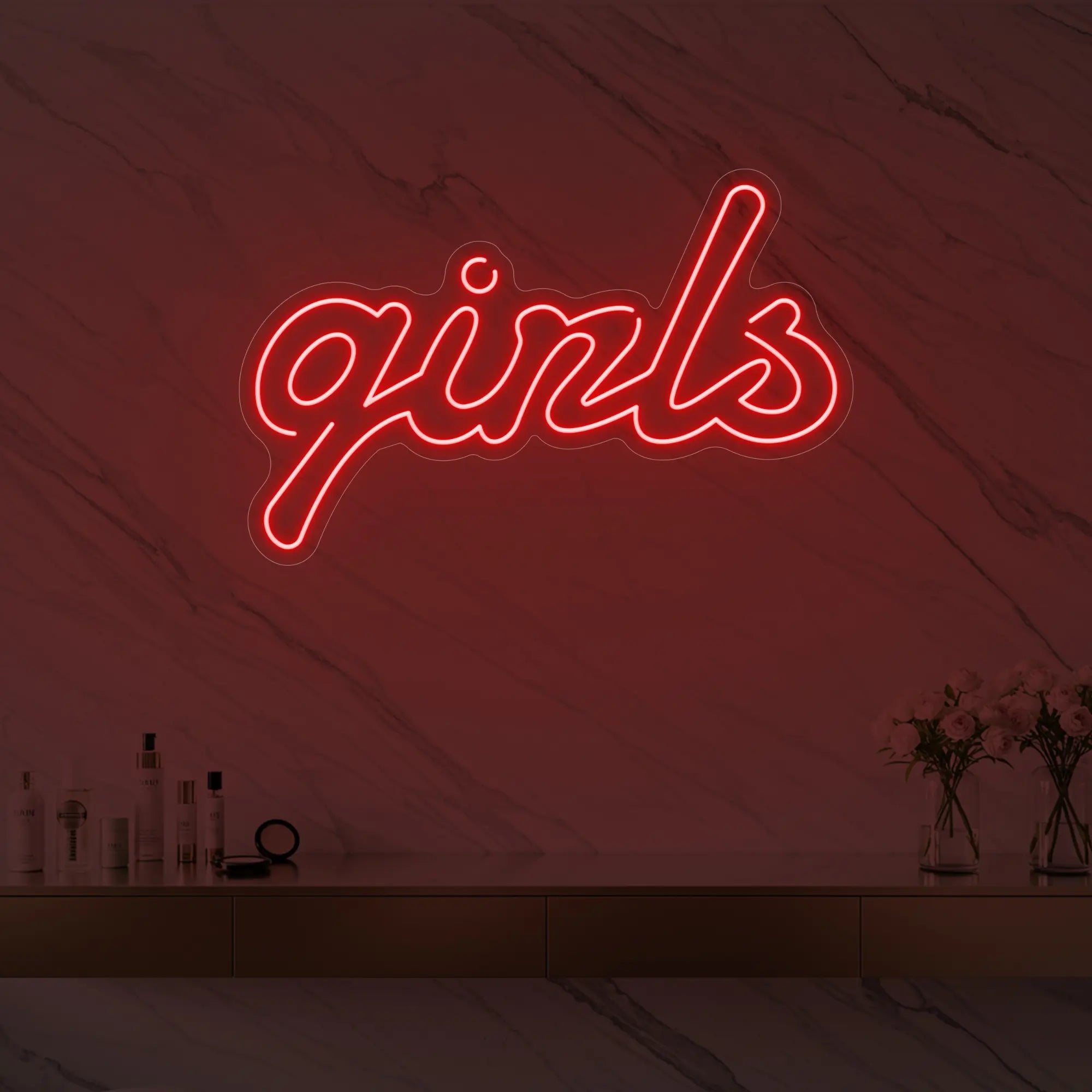 Photo of the 'girls' neon sign in playful script glowing in red against a styled interior wall.
