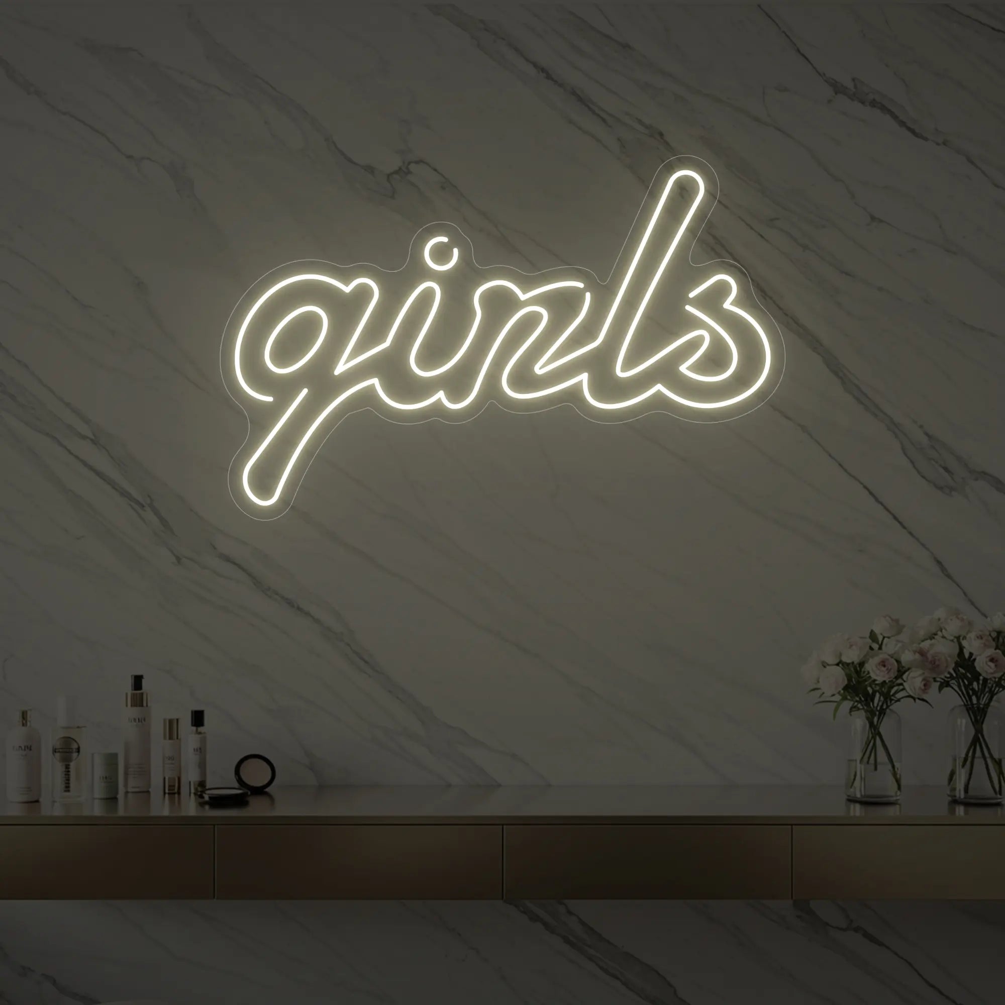 Photo of the 'girls' neon sign in playful script glowing in warm white against a styled interior wall.