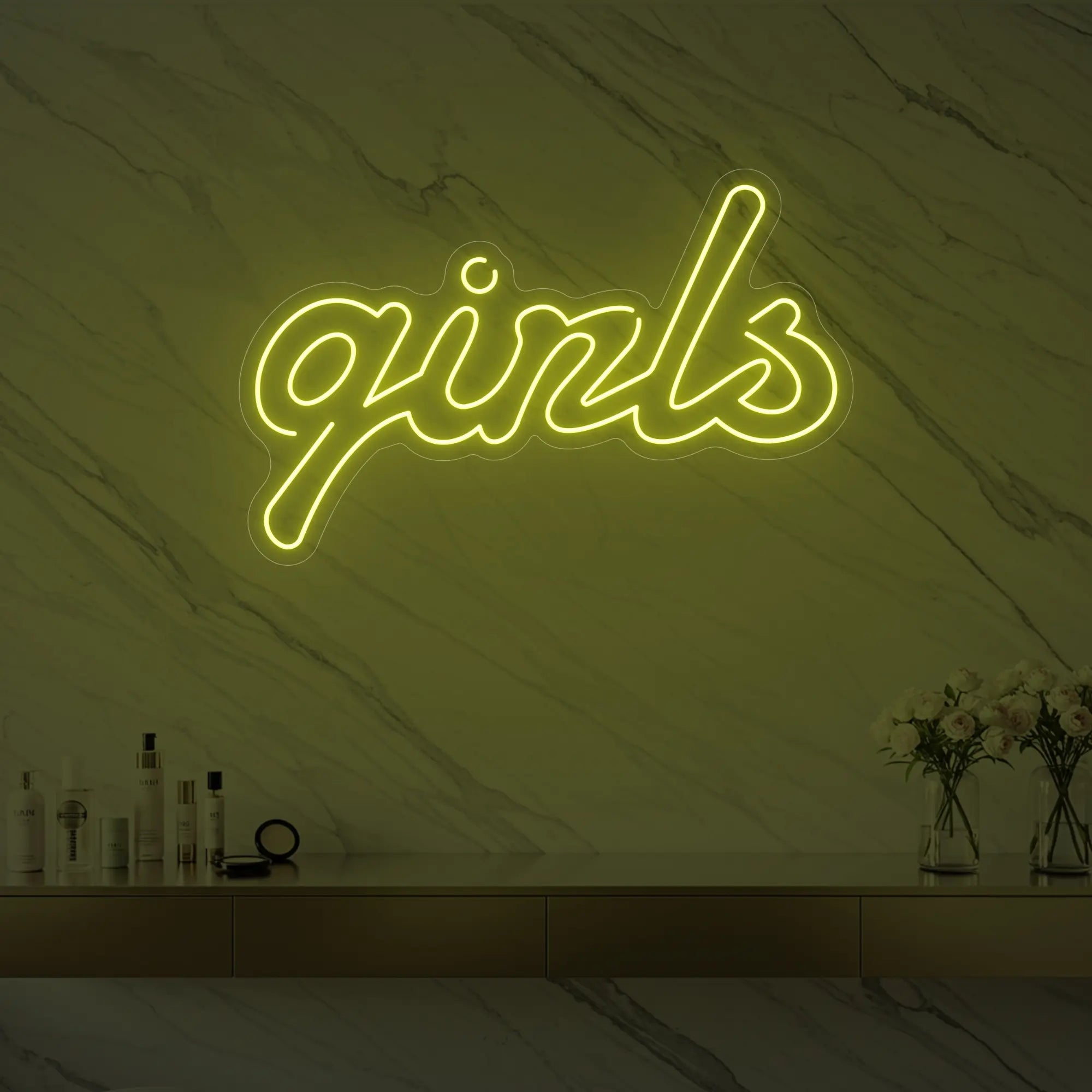 Photo of the 'girls' neon sign in playful script glowing in lemon yellow against a styled interior wall.