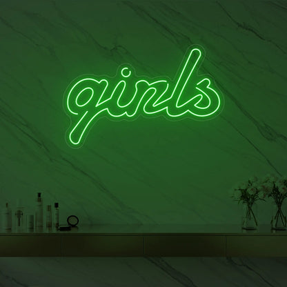 Photo of the 'girls' neon sign in playful script glowing in green against a styled interior wall.