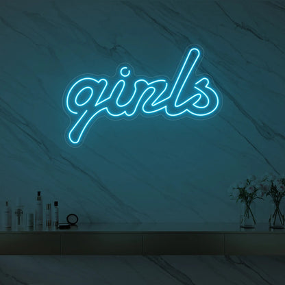 Photo of the 'girls' neon sign in playful script glowing in ice blue against a styled interior wall.