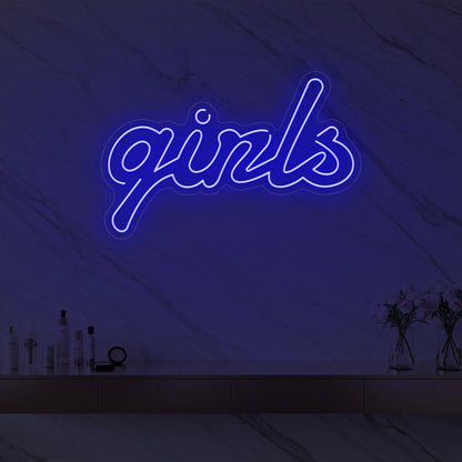 Photo of the 'girls' neon sign in playful script glowing in deep blue against a styled interior wall.