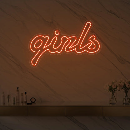 Photo of the 'girls' neon sign in playful script glowing in golden yellow against a styled interior wall.