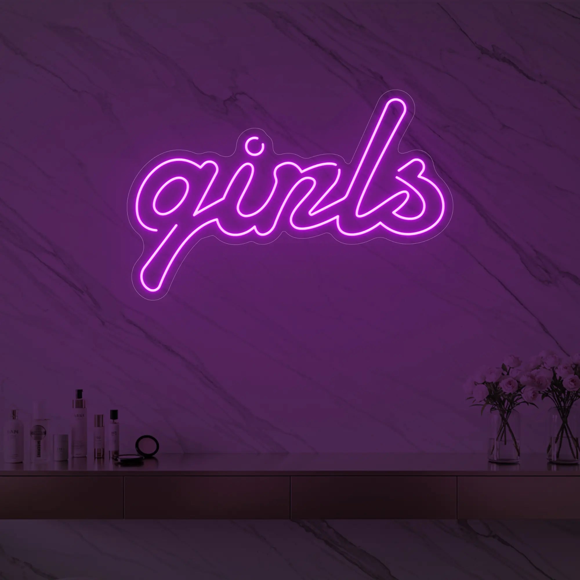 Photo of the 'girls' neon sign in playful script glowing in deep pink against a styled interior wall.