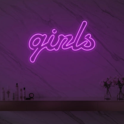 Photo of the 'girls' neon sign in playful script glowing in deep pink against a styled interior wall.