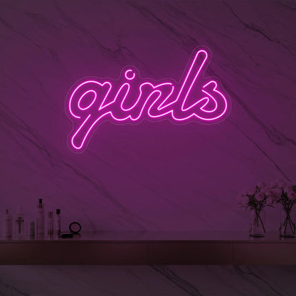 Photo of the 'girls' neon sign in playful script glowing in light pink against a styled interior wall.