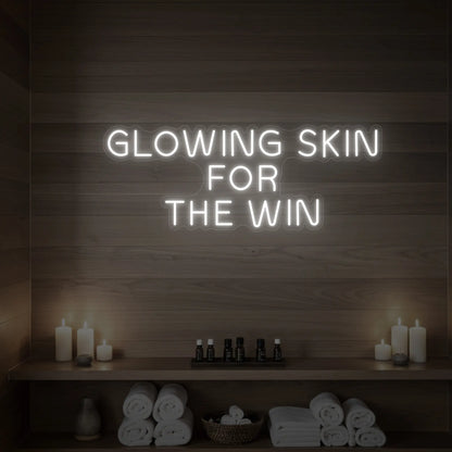 Photo of the 'GLOWING SKIN FOR THE WIN' neon sign glowing in cool white against a styled interior wall.