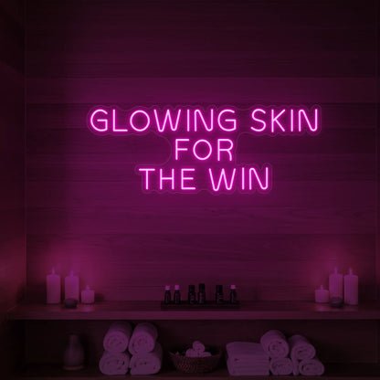 Photo of the 'GLOWING SKIN FOR THE WIN' neon sign glowing in light pink against a styled interior wall.