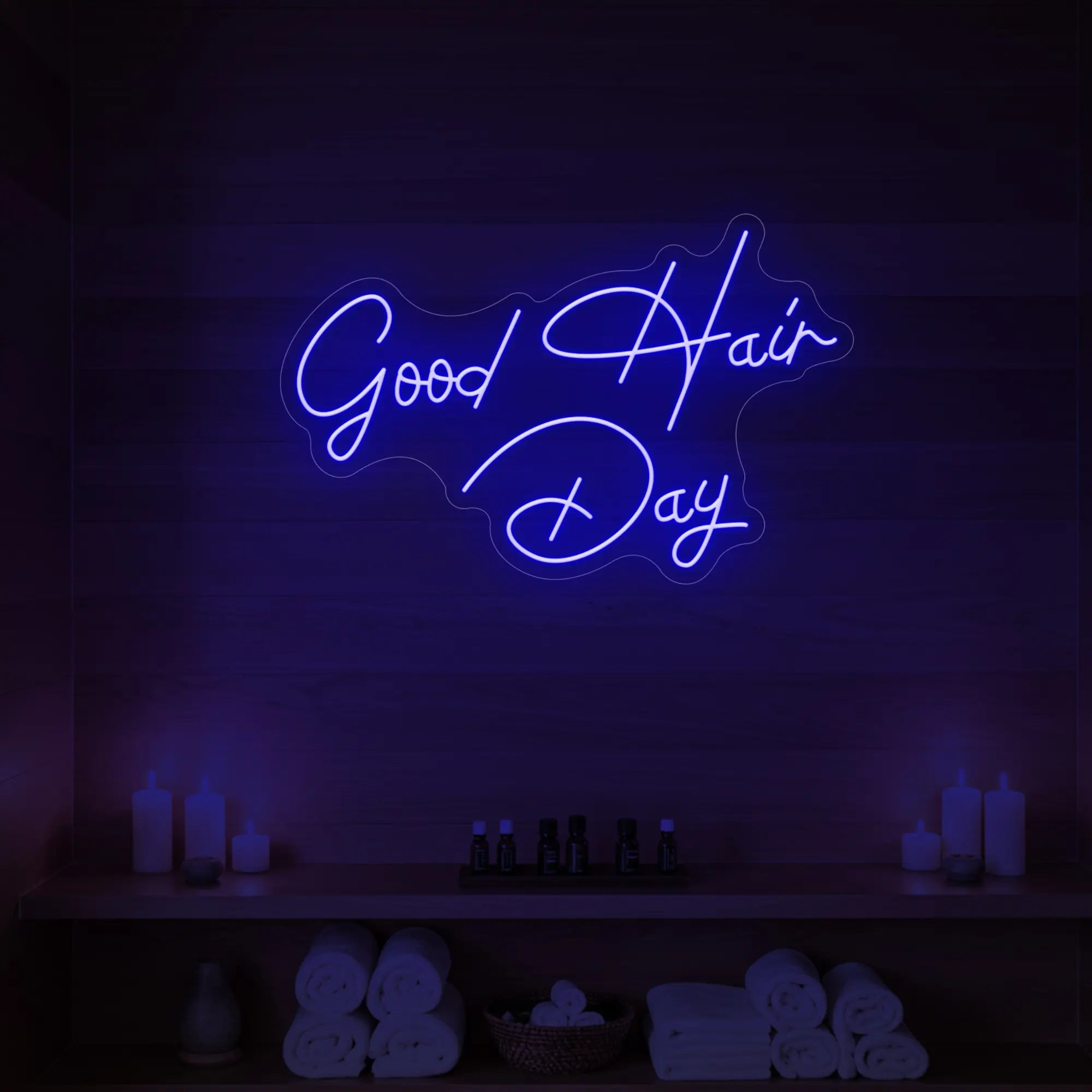 Photo of the 'Good Hair Day' neon sign in cursive glowing in deep blue against a styled interior wall.