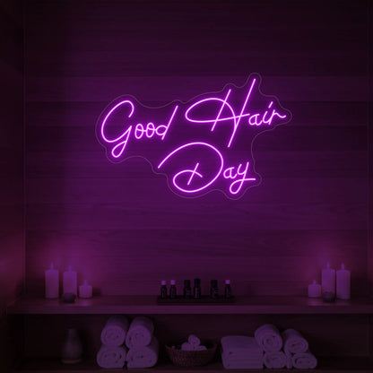 Photo of the 'Good Hair Day' neon sign in cursive glowing in deep pink against a styled interior wall.